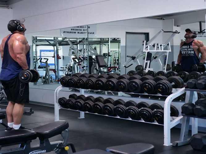 A man wearing headphones is lifting dumbbells in a gym