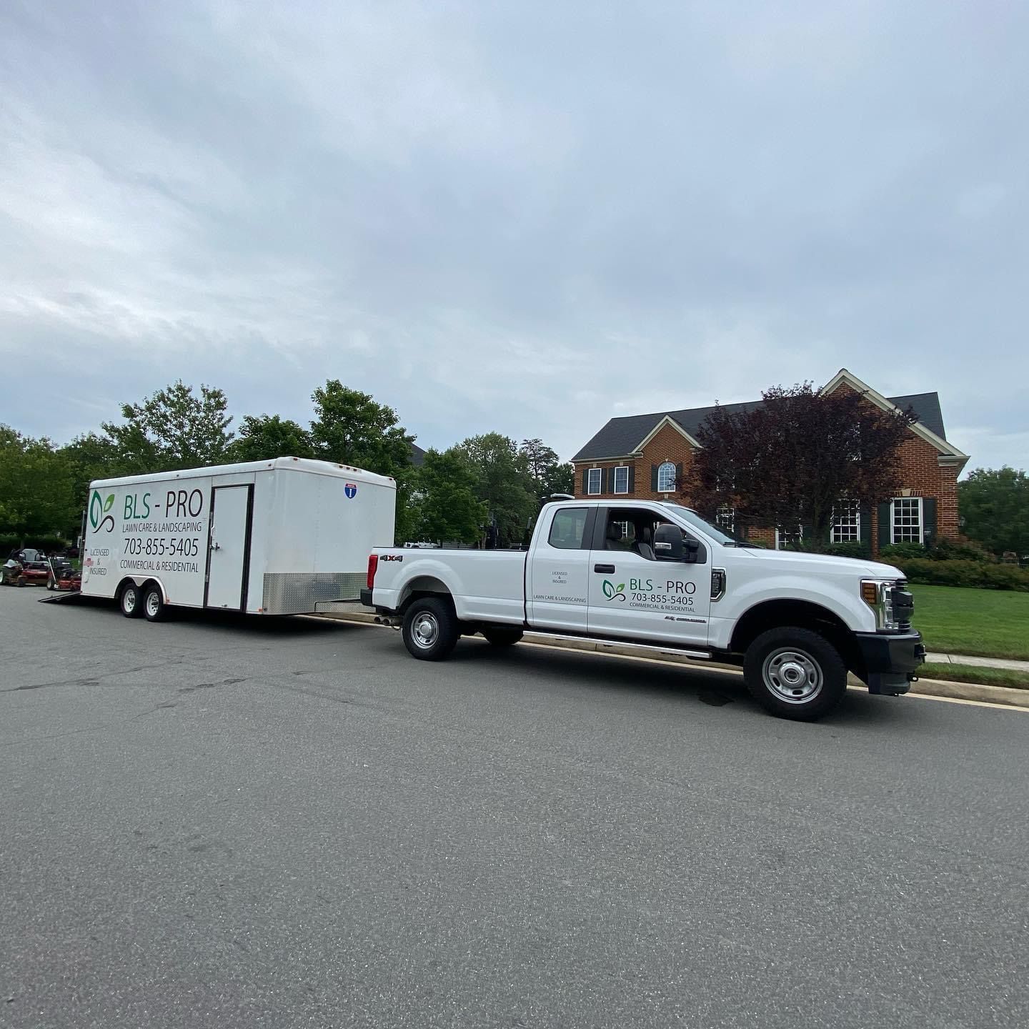 Camión blanco remolcando un remolque en una calle residencial; el camión y el remolque tienen logotipos de 