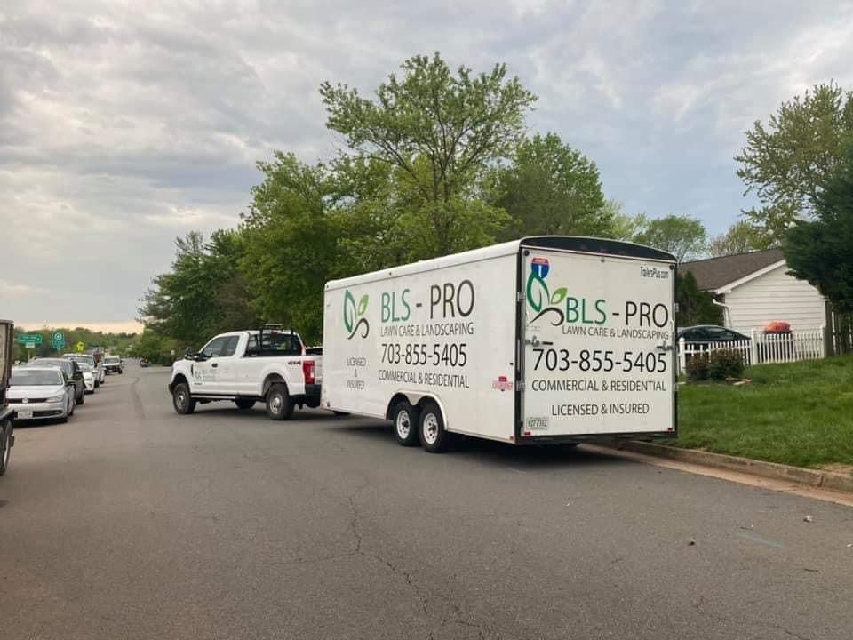 Camioneta blanca que arrastra un remolque con el logotipo de servicios de jardinería 