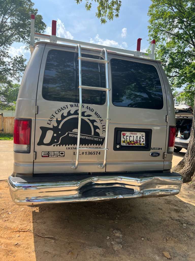 Parte trasera de una camioneta de trabajo plateada con una escalera en la parte superior y un logotipo de 