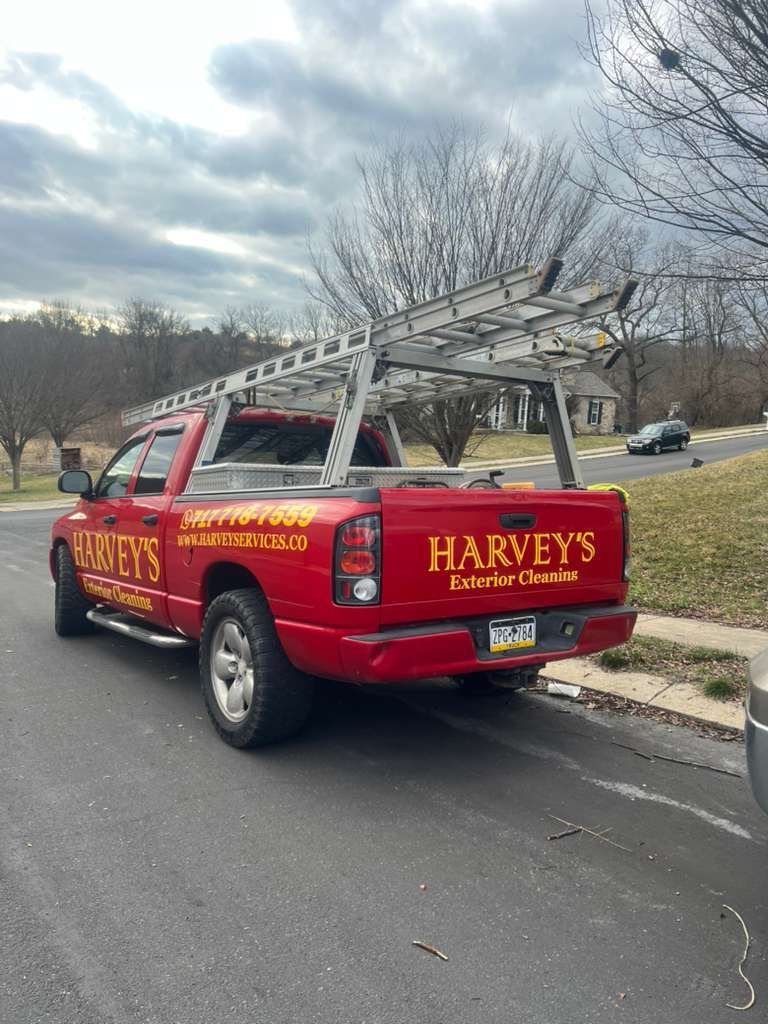 La camioneta de Red Harvey con portaescaleras estacionada sobre asfalto. Letras amarillas. Día nublado.