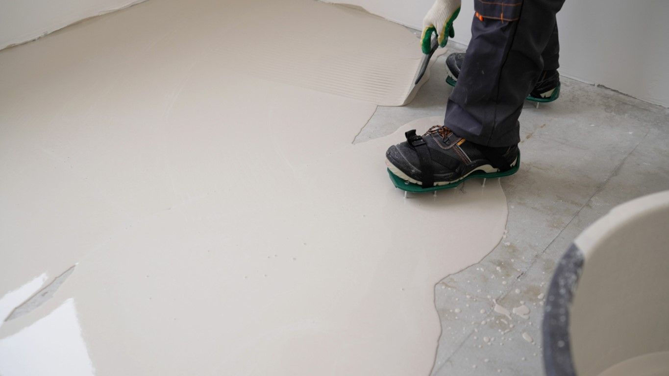 Person smoothing floor leveling compound with a trowel. White compound covers floor.