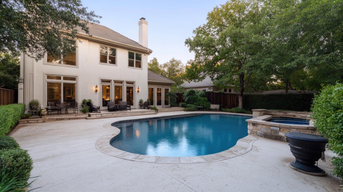 Backyard with pool, patio, and two-story house. Trees surround the area; the house has large windows.