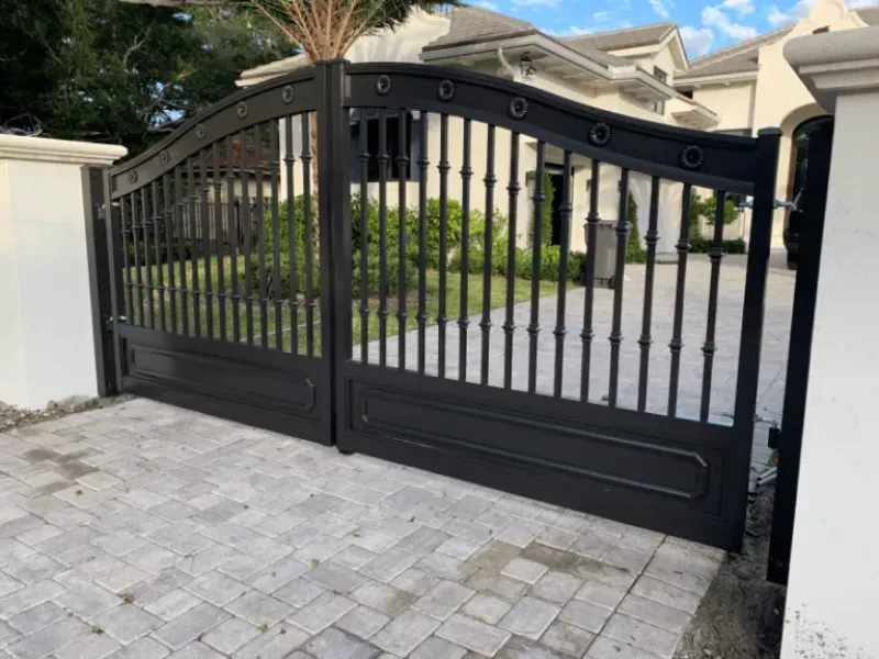 A black gate is open to a driveway in front of a house.