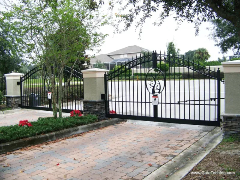 A wrought iron gate is open to a driveway in front of a house