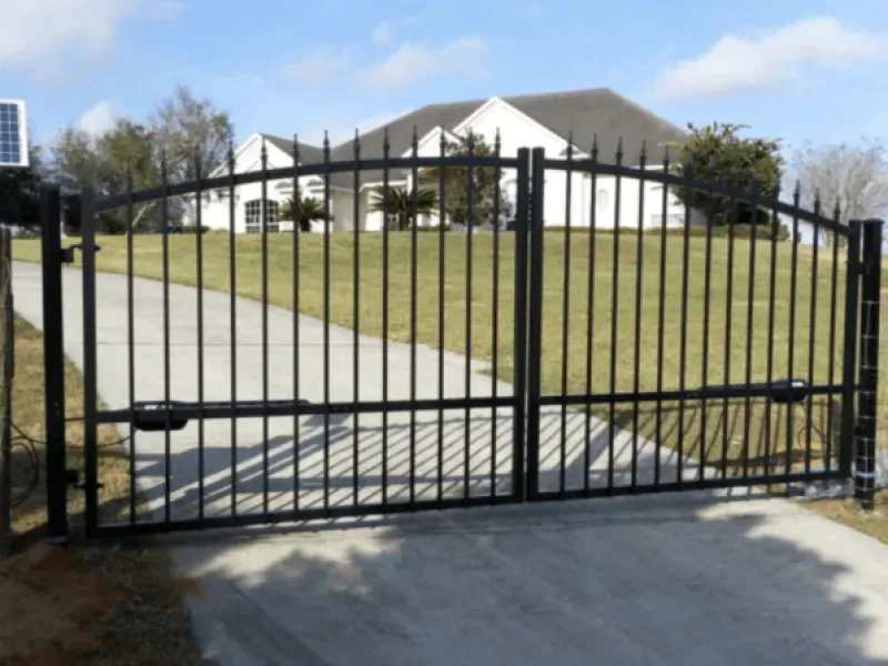 A black gate is open to a driveway with a house in the background
