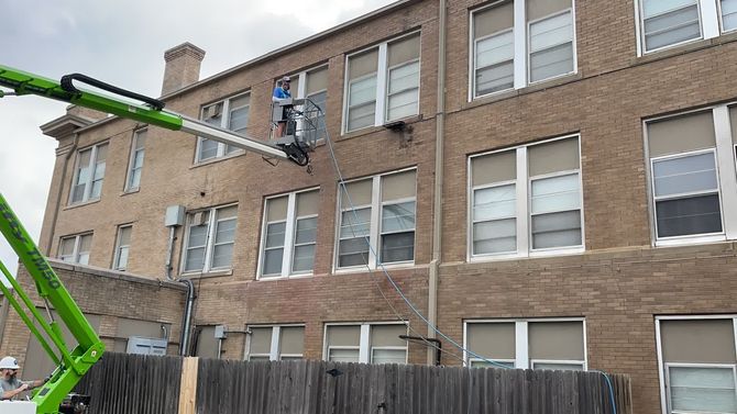 A green crane is cleaning the windows of a brick building. A green crane is cleaning the windows of a brick building.