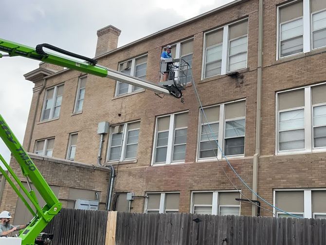A green crane is cleaning the windows of a brick building. A green crane is cleaning the windows of a brick building.