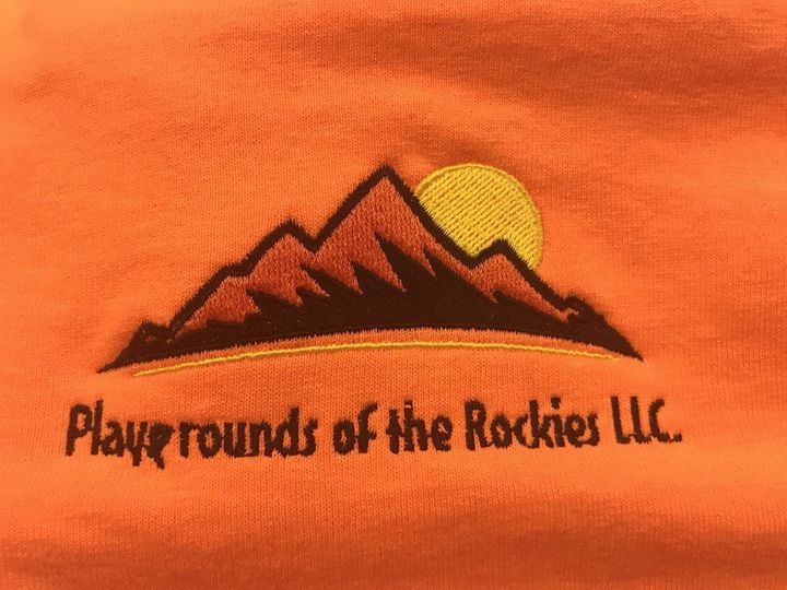Embroidered logo on orange fabric: stylized dark brown mountains with a yellow sun, above the text 