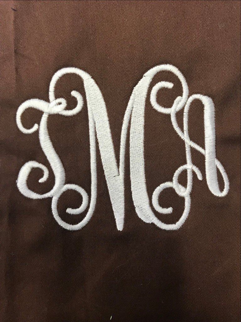White embroidered monogram on a dark brown fabric background, featuring the letters 