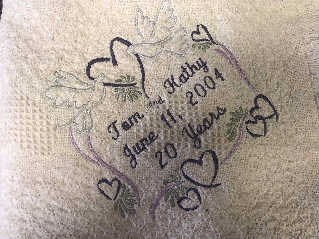 Embroidered white fabric featuring two doves, hearts, and the text 