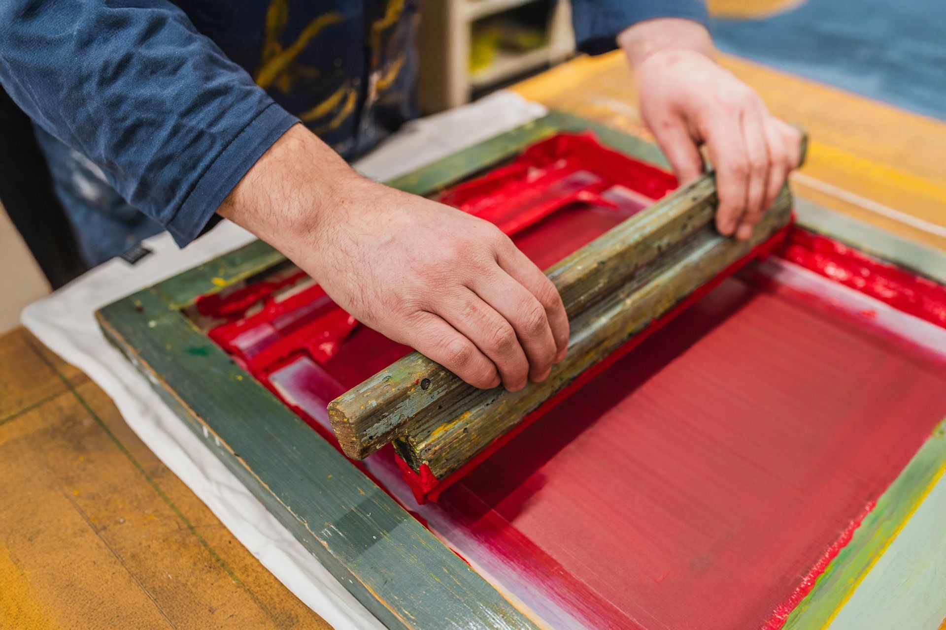 A person uses a squeegee to pull red ink across a screen printing frame.