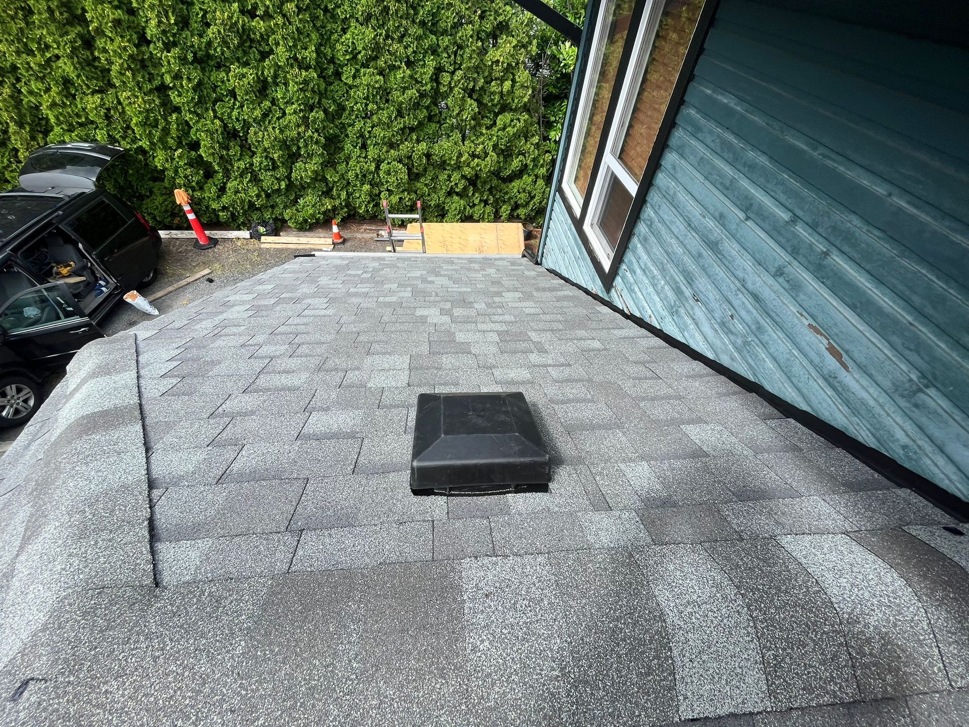 A black box is sitting on top of a roof next to a blue house.