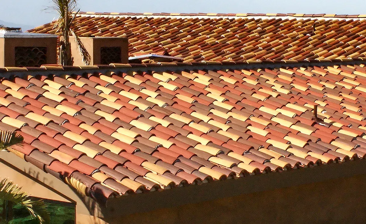 A roof with a vent on it and a building in the background.