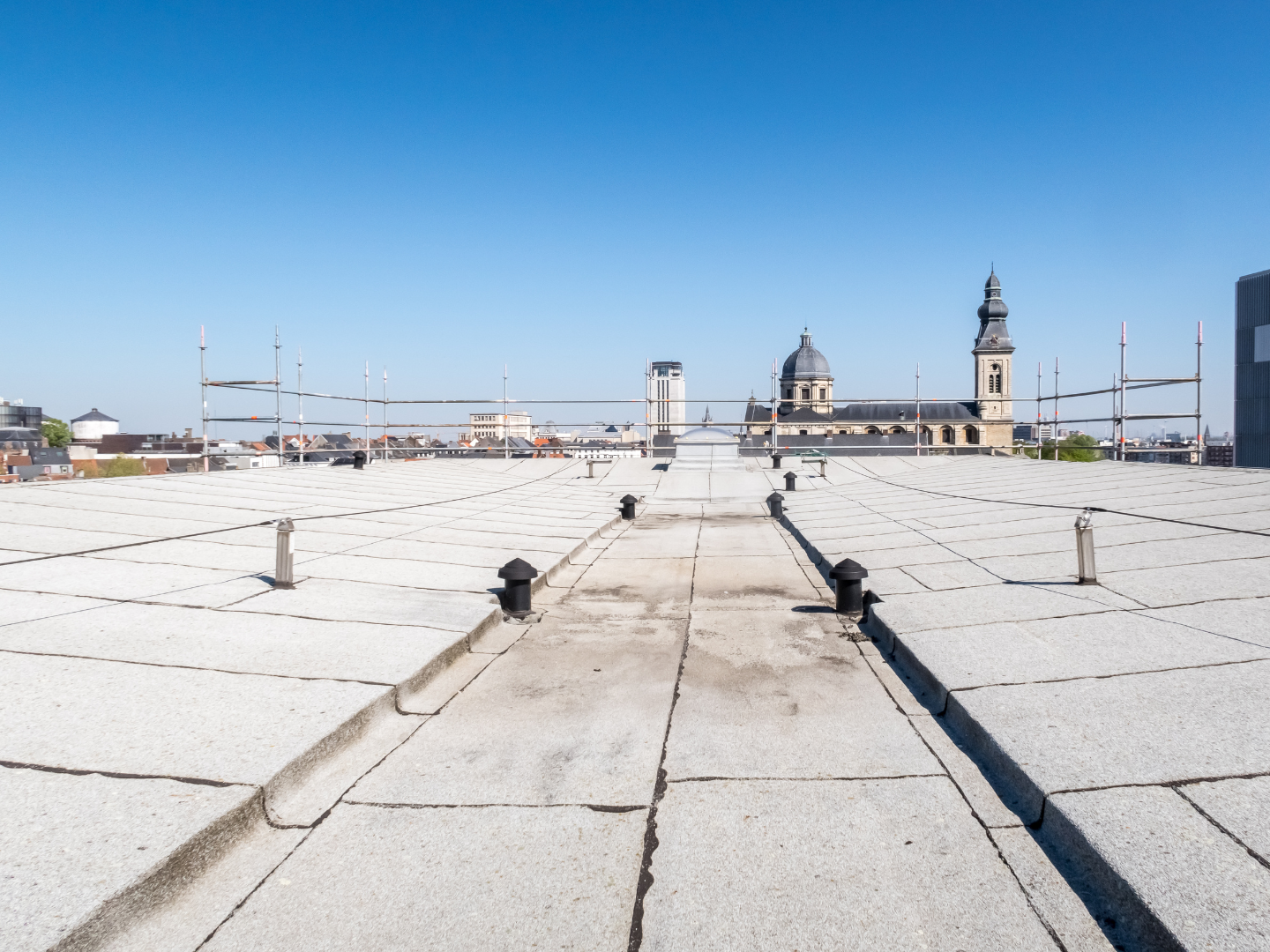 A roof with a vent on it and a building in the background.