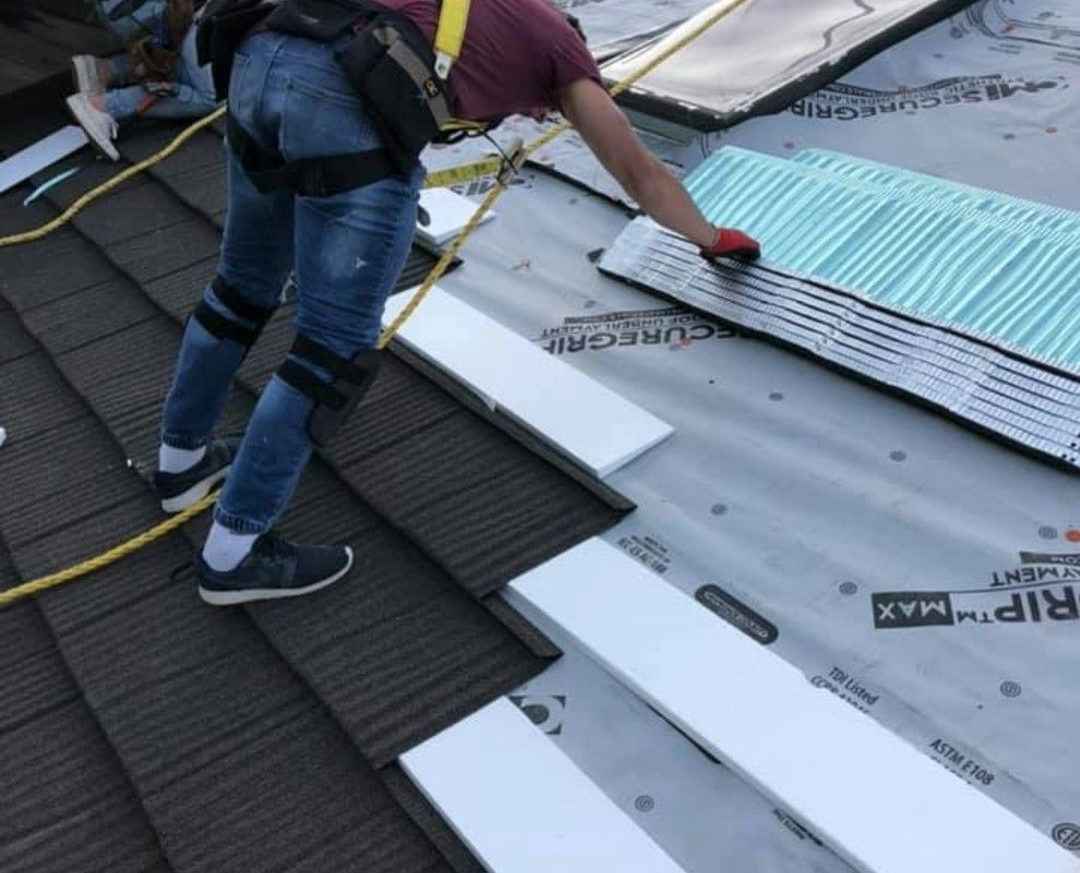 A roof with a vent on it and a building in the background.
