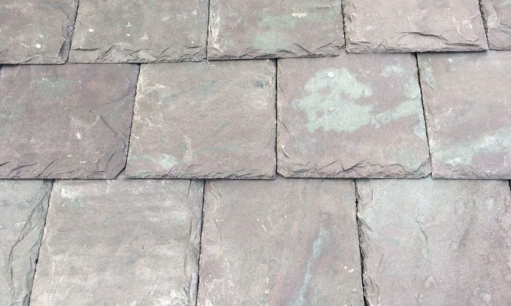 A roof with a vent on it and a building in the background.