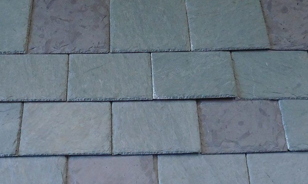 A roof with a vent on it and a building in the background.