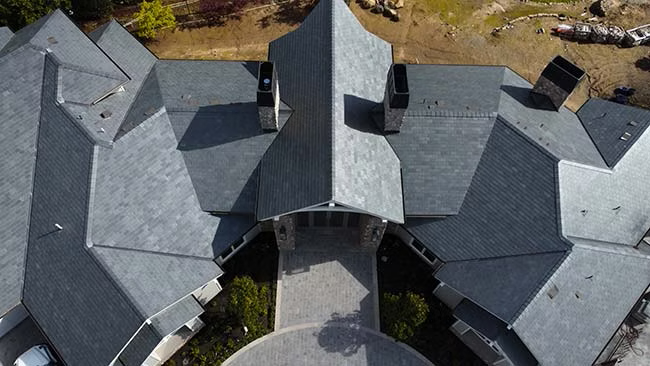 A roof with a vent on it and a building in the background.