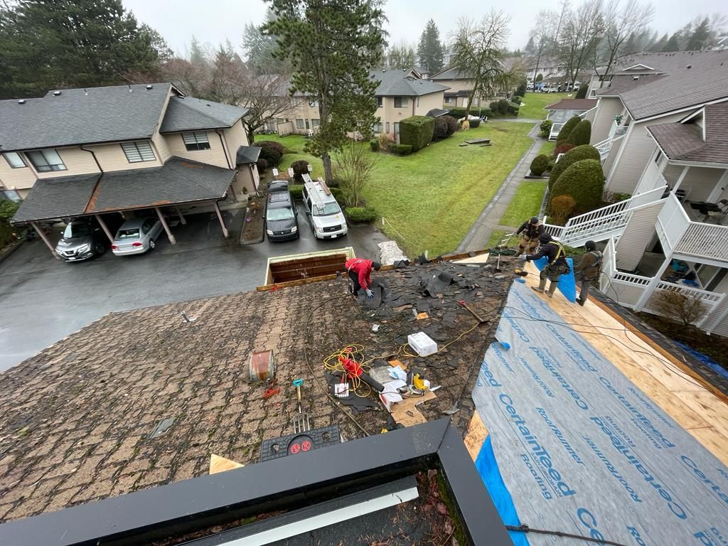 Workers replacing a shingle roof on a townhouse; tools and materials scattered.