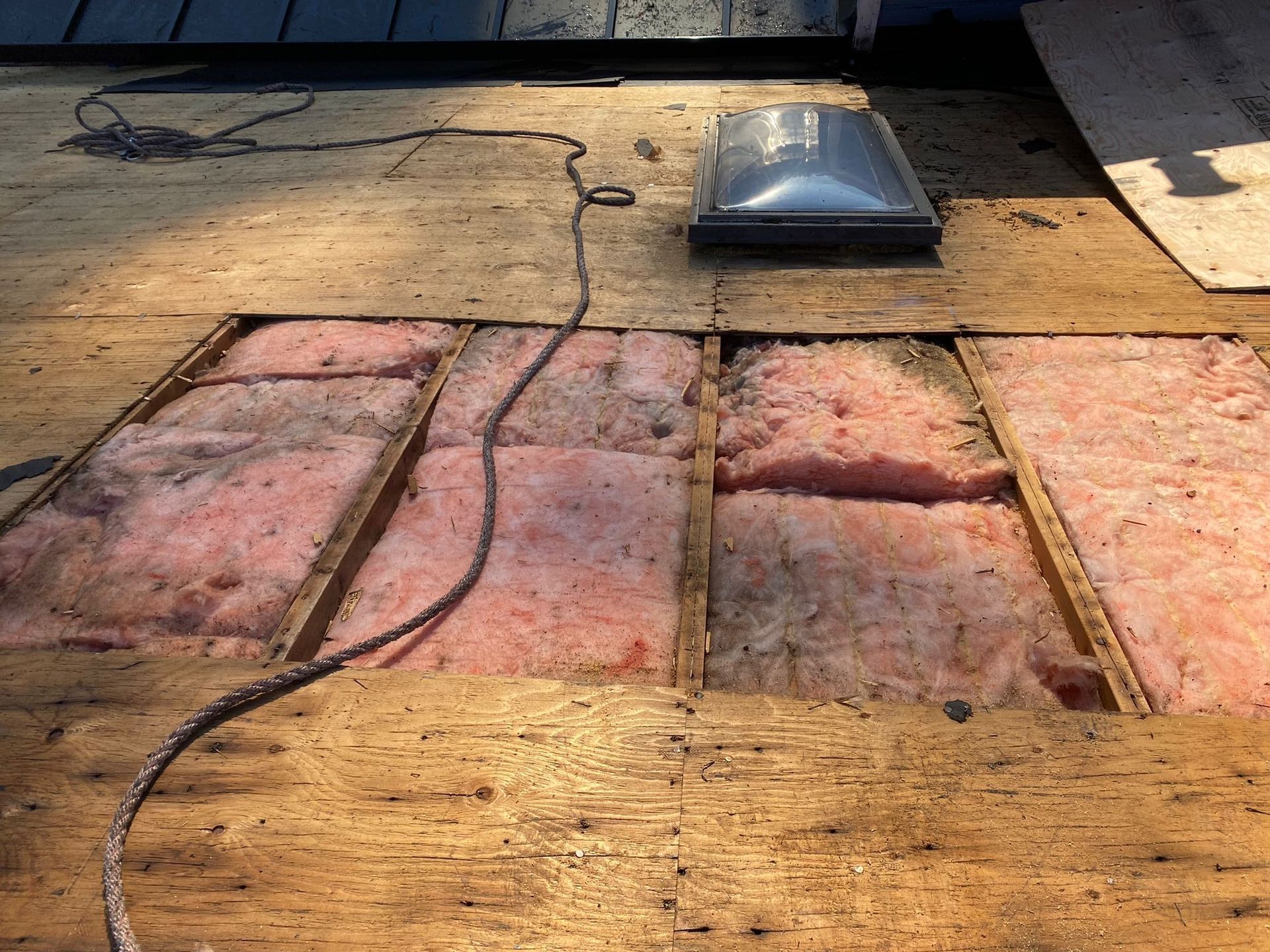 Roof opening exposing pink insulation and skylight on a sunny day.