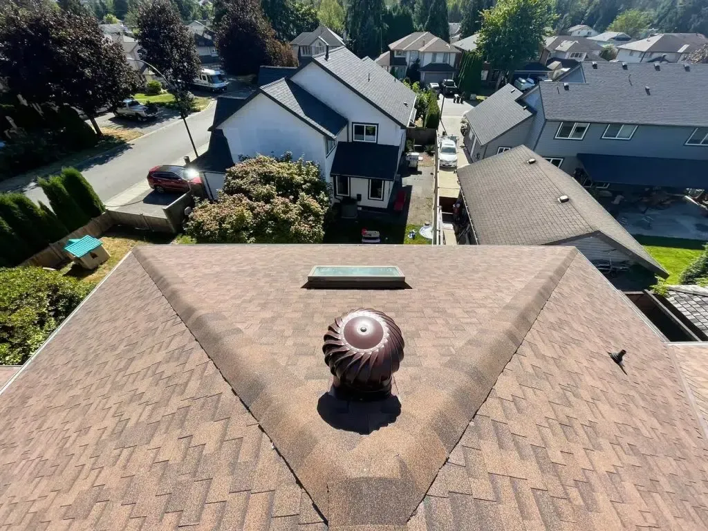 Rooftop view of several houses with asphalt shingle roofs and spinning turbine vents on a sunny day.
