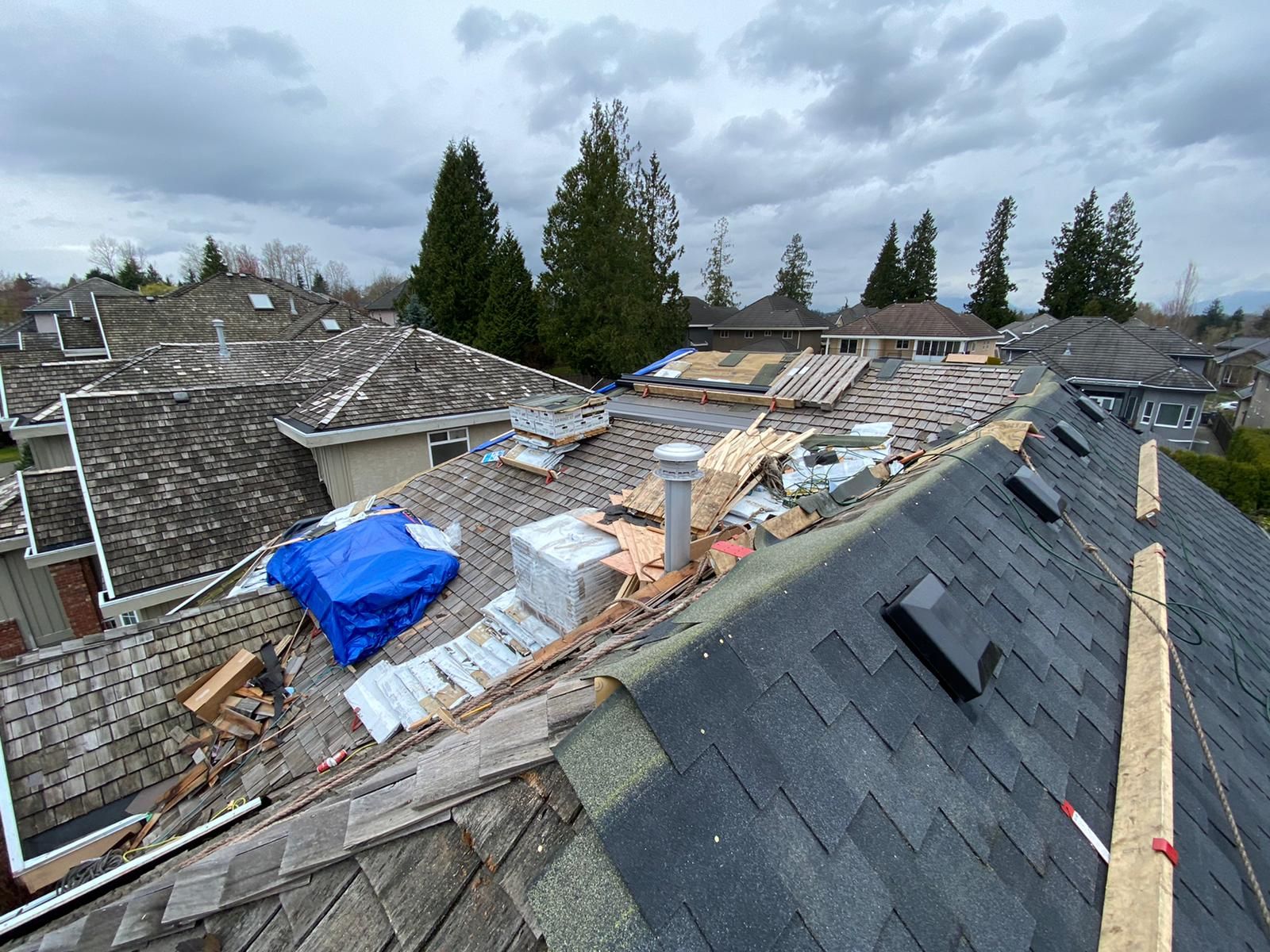The roof of a house is being repaired and there is a blue tarp on the roof.