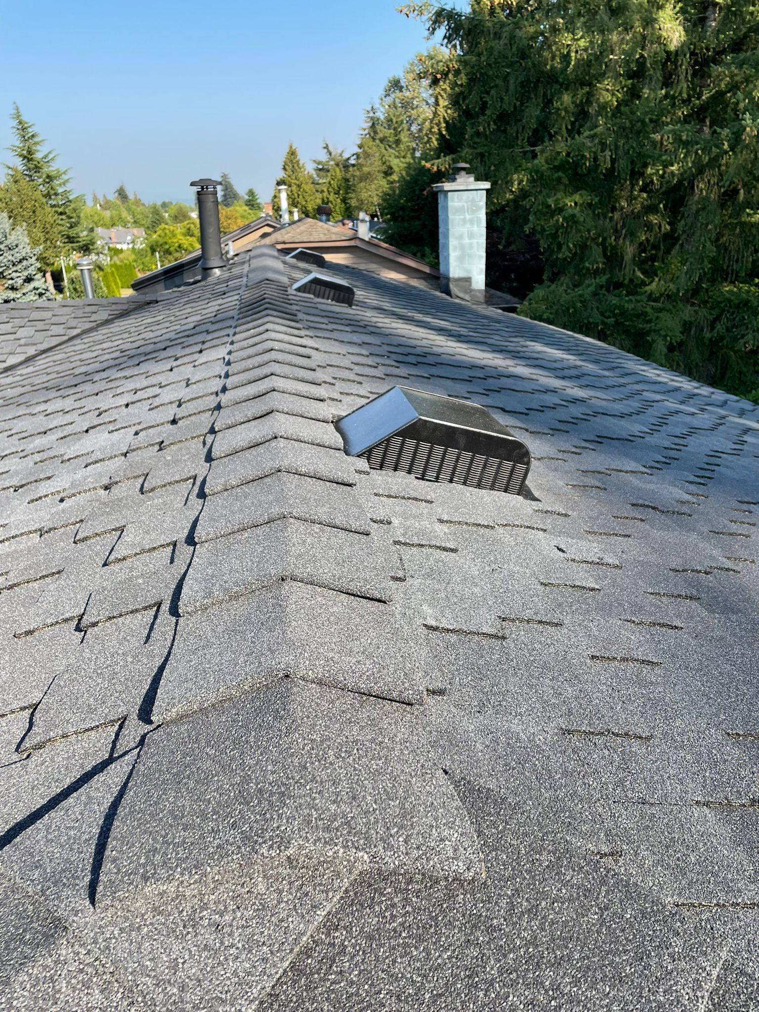A roof with a vent on it and trees in the background.