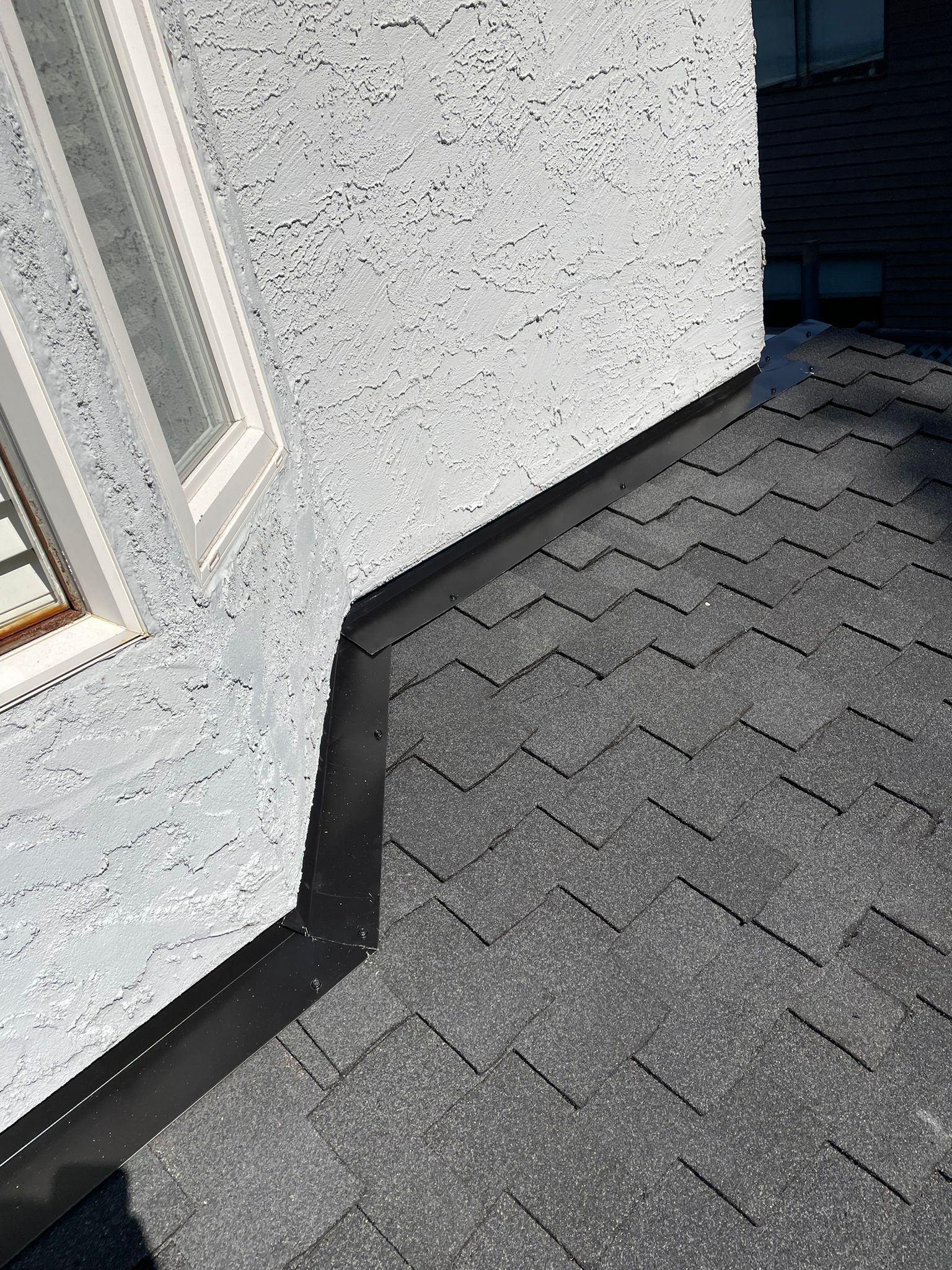 A corner of a building with a black roof and a window.