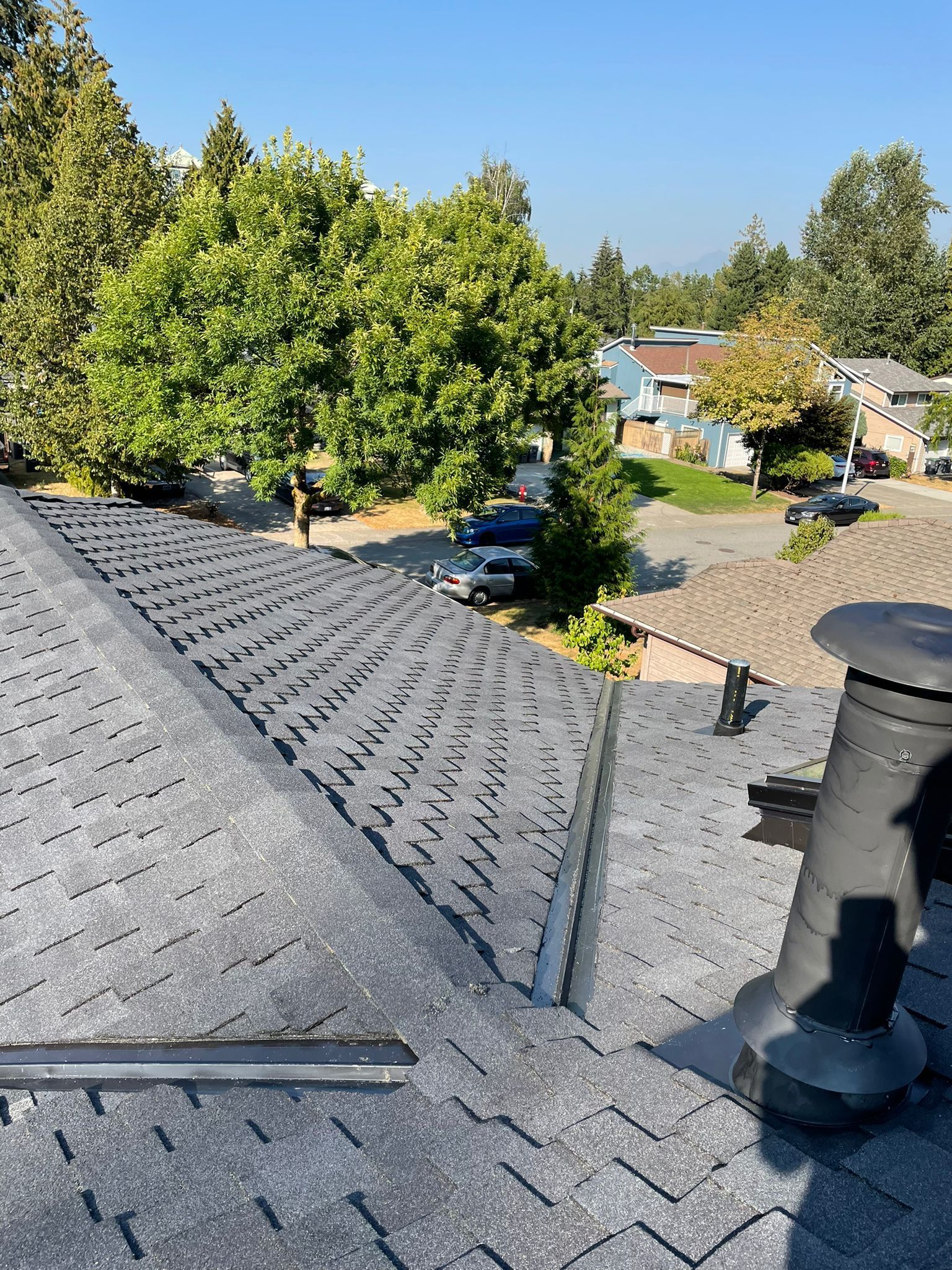 A roof with a chimney on it and trees in the background.
