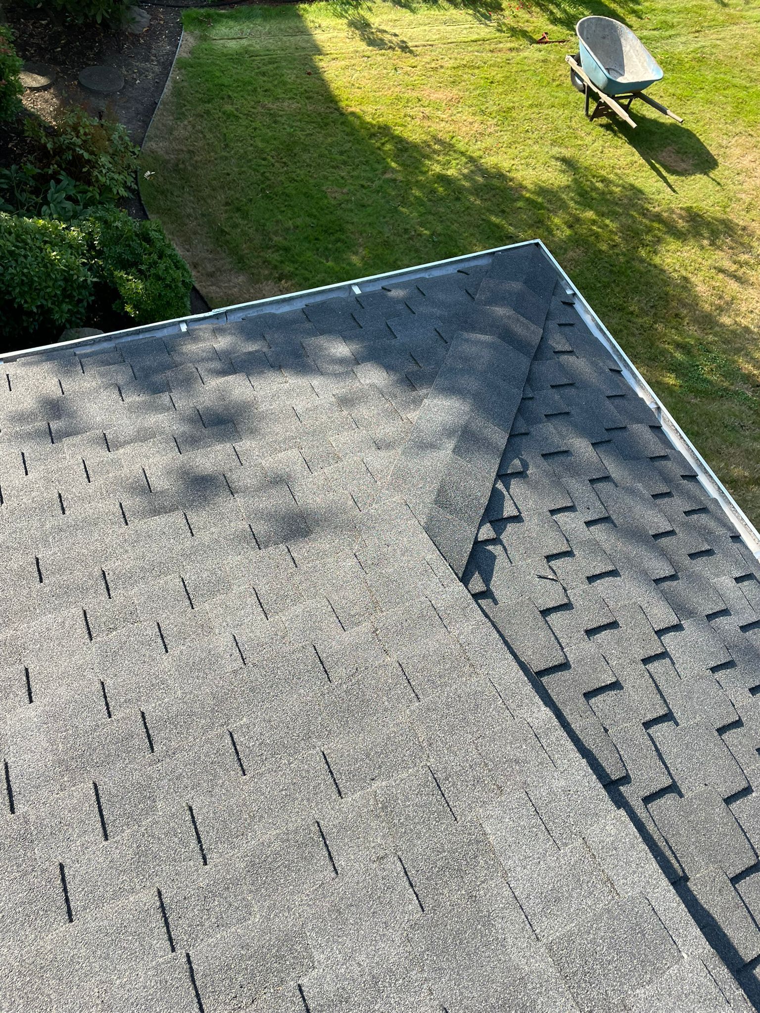 An aerial view of a roof with shingles and a wheelbarrow in the background.