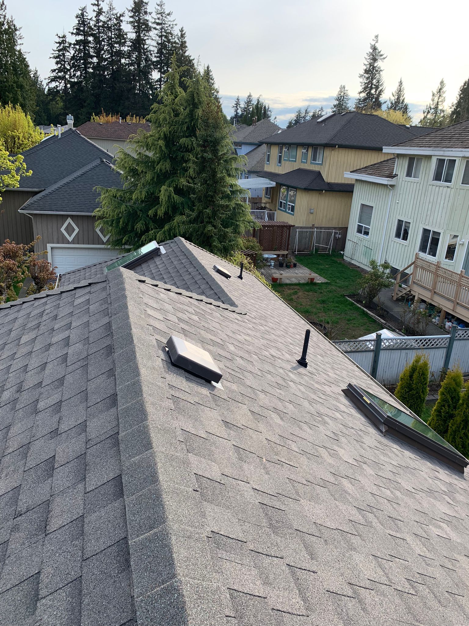 View of a gray shingle roof with vents, overlooking suburban houses and trees.