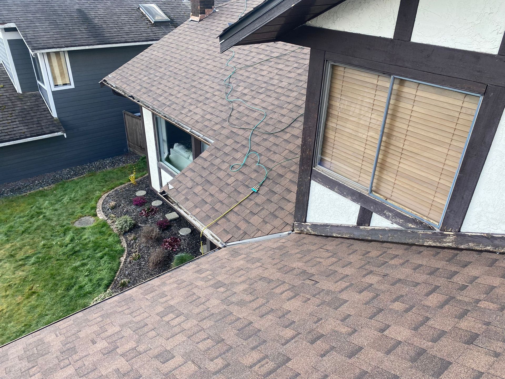 Brown shingle roof of a house with visible cracks near a window with bamboo blinds.