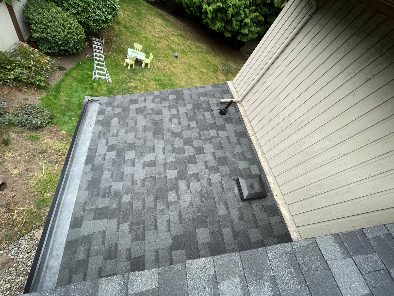 An aerial view of a roof of a house with a table and chairs in the backyard.