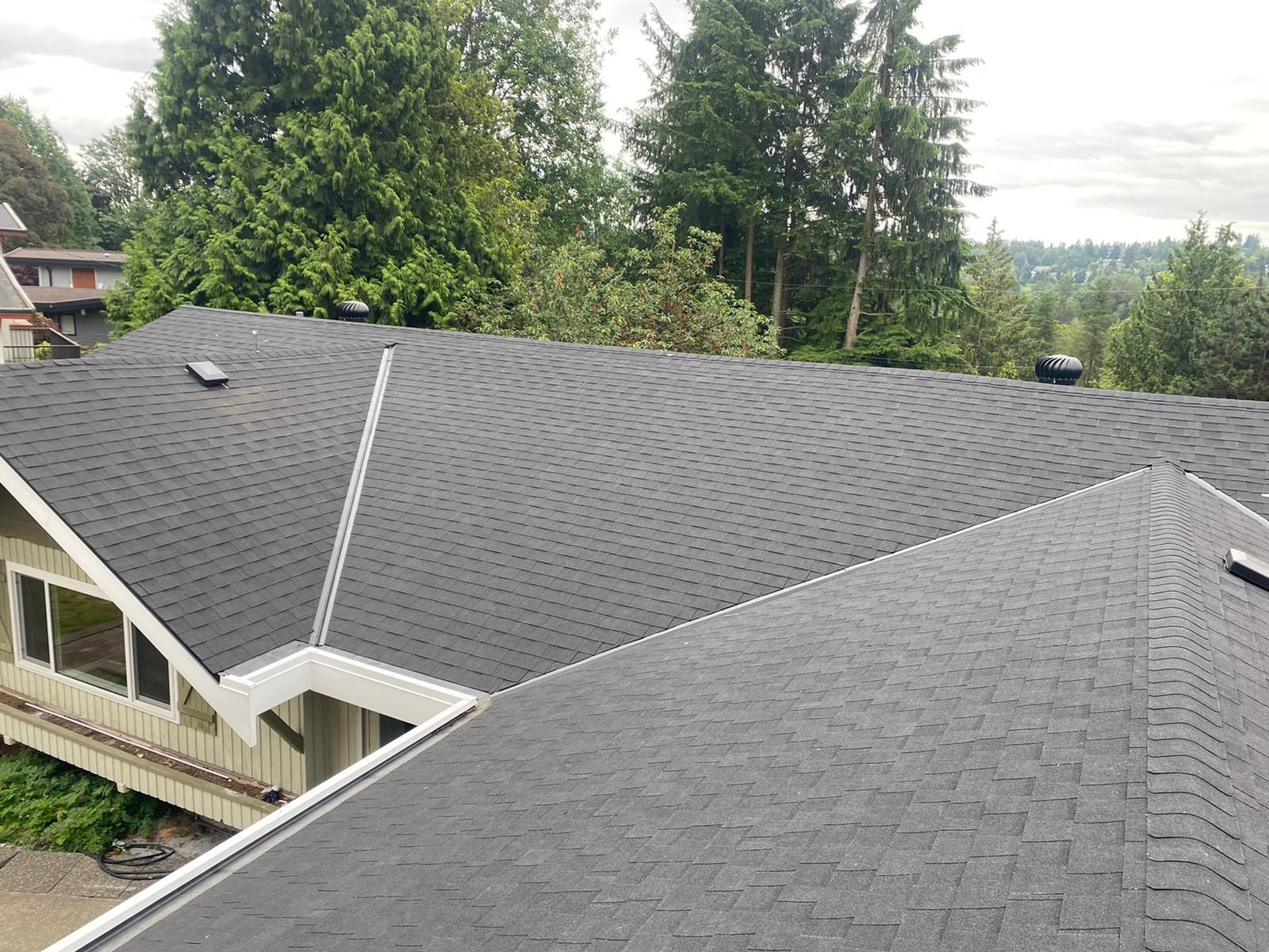An aerial view of a house with a black roof and trees in the background.