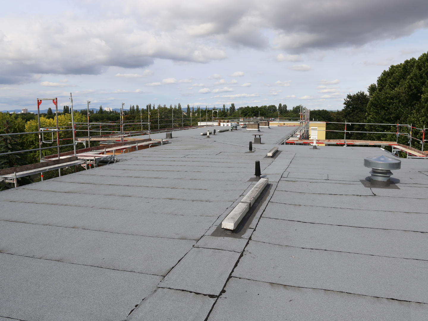 A roof with a vent on it and a building in the background.