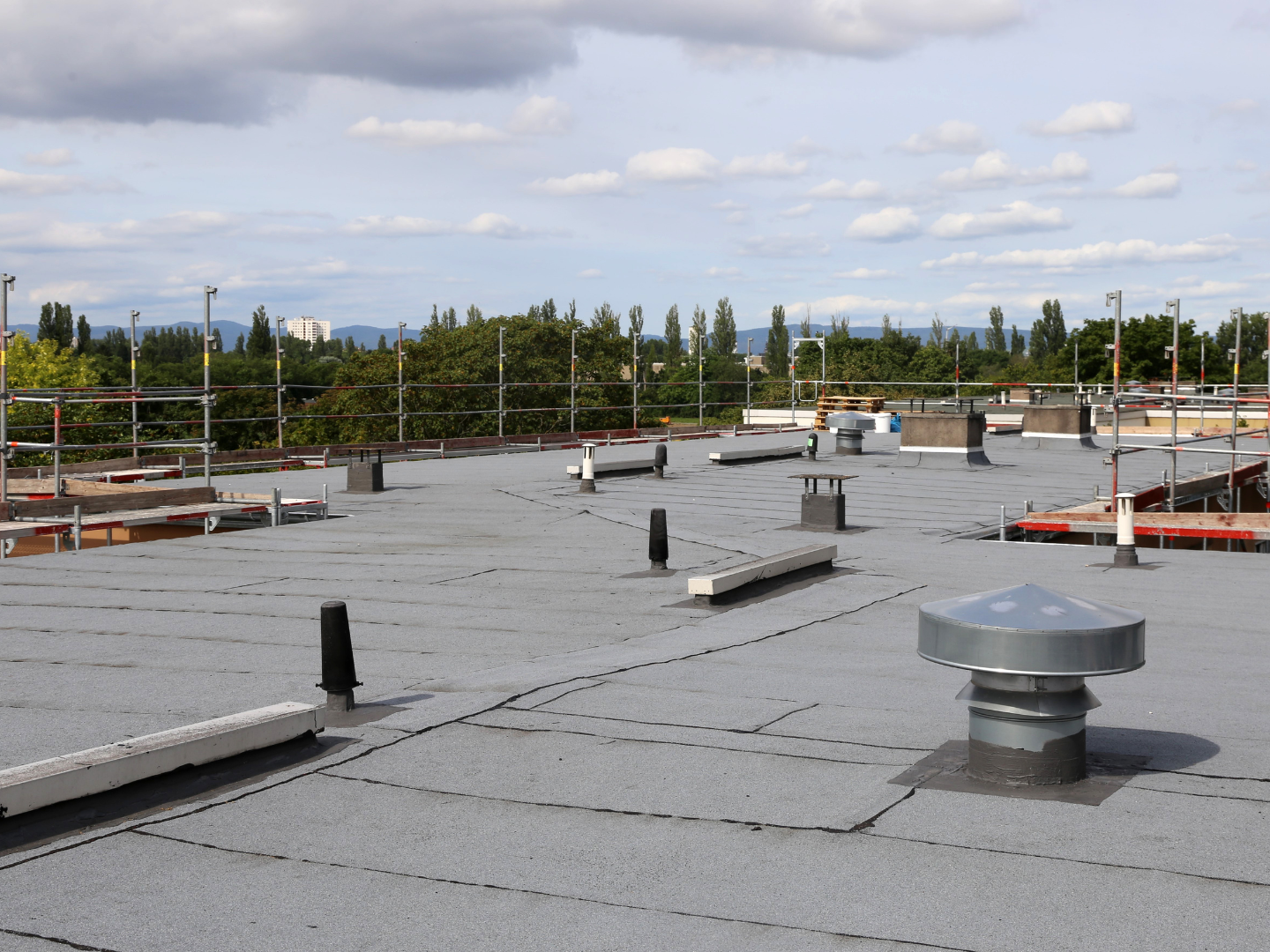A roof with a vent on it and a building in the background.