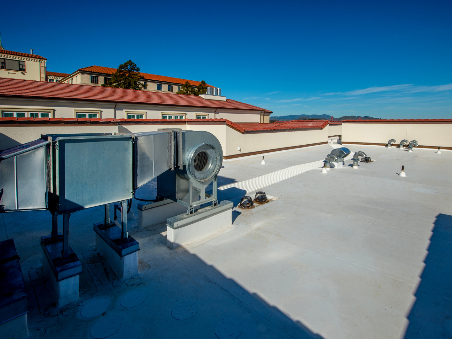 A roof with a vent on it and a building in the background.
