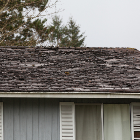 A roof with a vent on it and a building in the background.