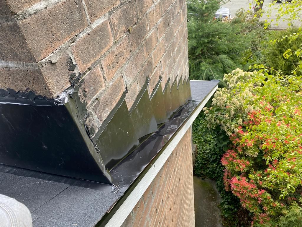 A roof with a vent on it and a building in the background.
