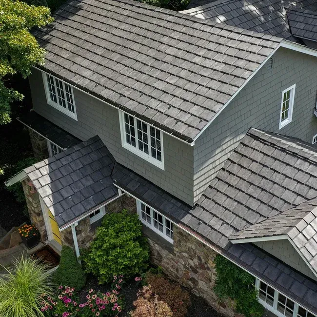 Wooden shingle roof with a central ridge, skylight, and chimneys on a building.