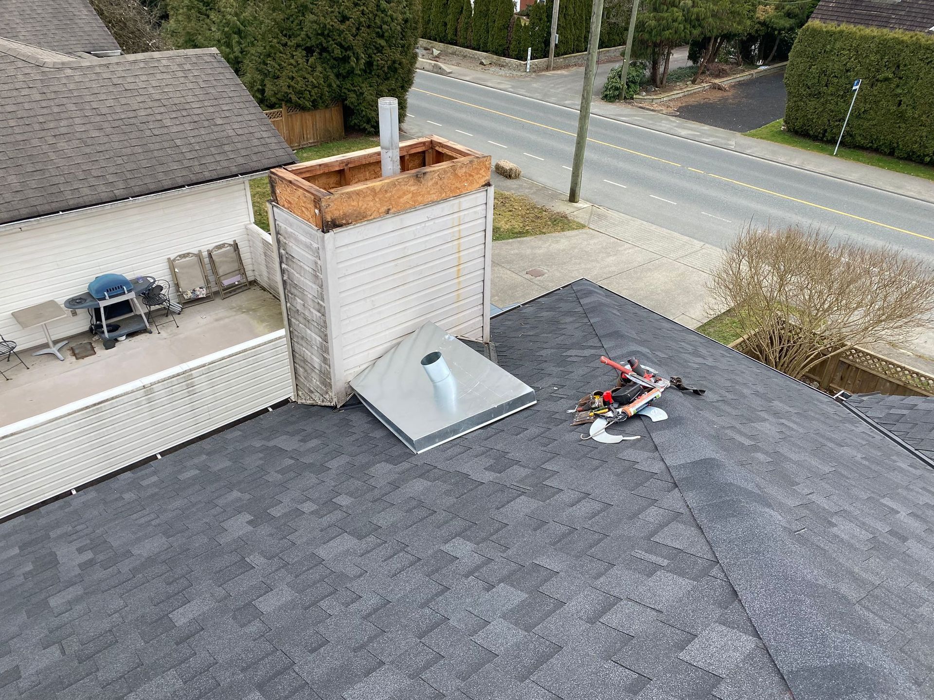 A roof with a vent on it and a building in the background.