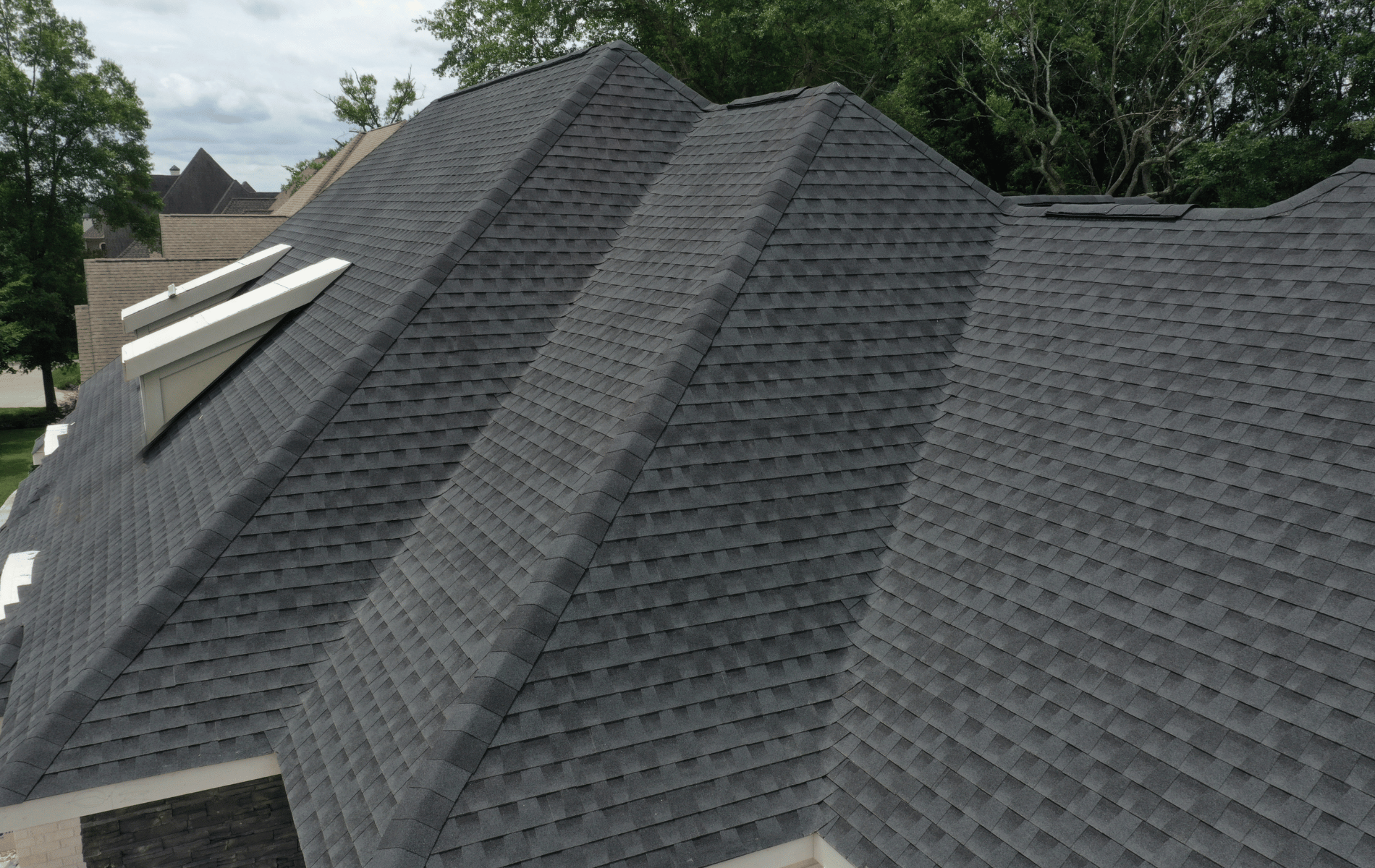 Dark gray asphalt shingle roof of a house with a multi-gabled design and skylights.