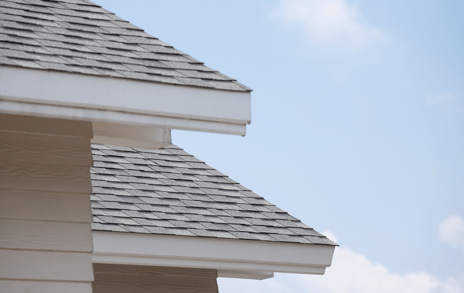 Close-up of a white house's roof and siding against a light blue sky.