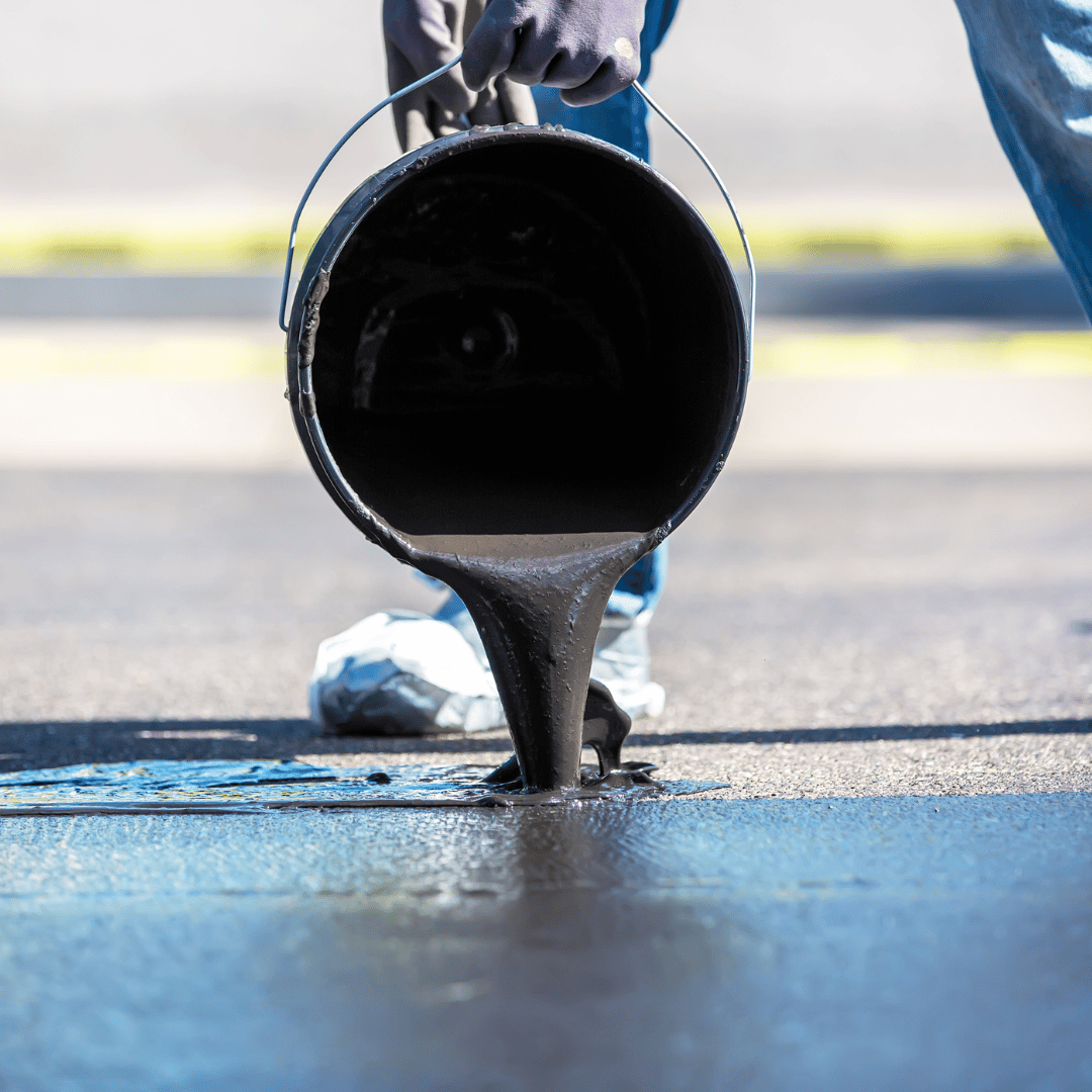 A person is pouring asphalt from a bucket onto the ground.