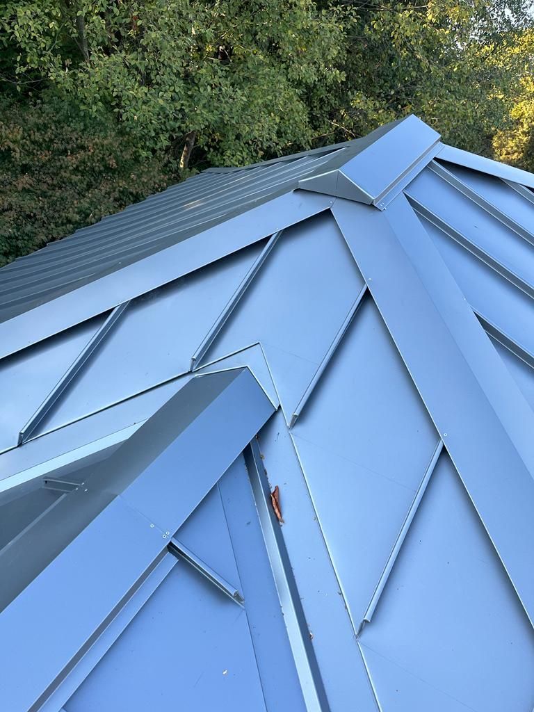 Gray metal roof with geometric design, trees in background.