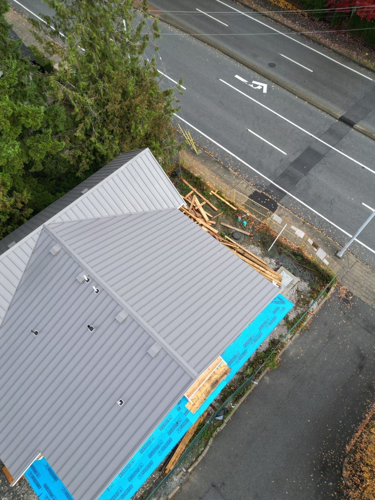 An aerial view of a building with a gray metal roof under construction next to a road.