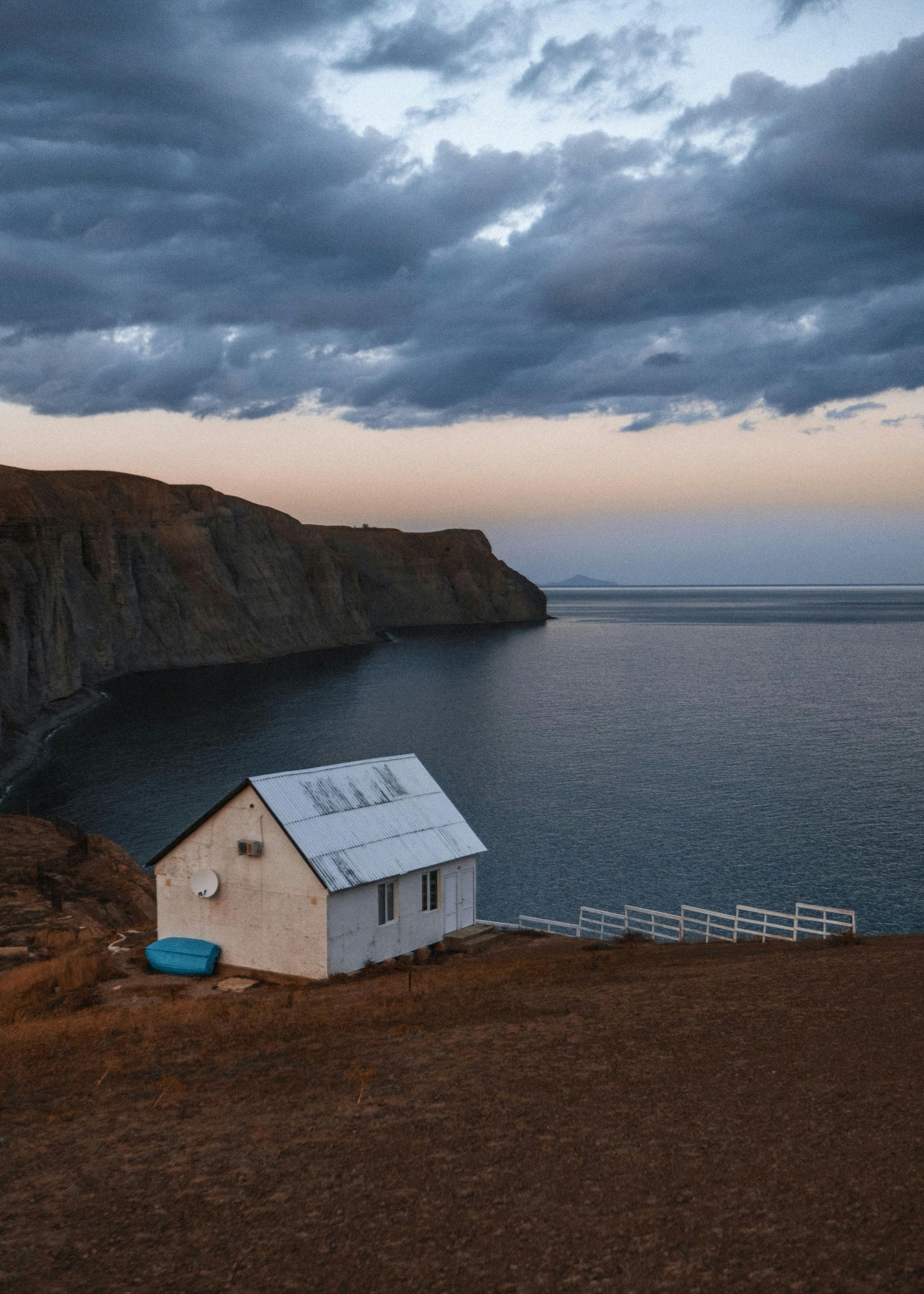 A small white house is sitting on the edge of a cliff overlooking the ocean.