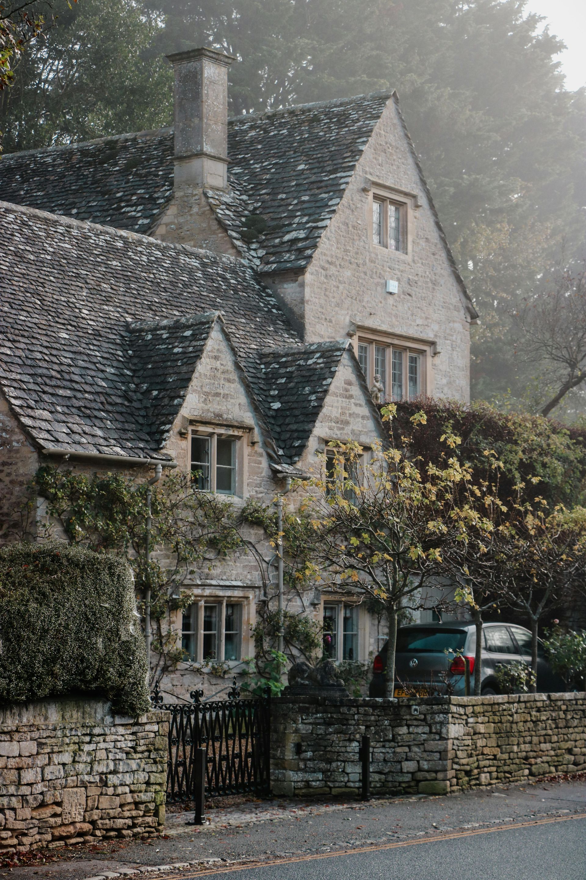 A large stone house with a slate roof is surrounded by trees and a stone wall., paragon roofing bc