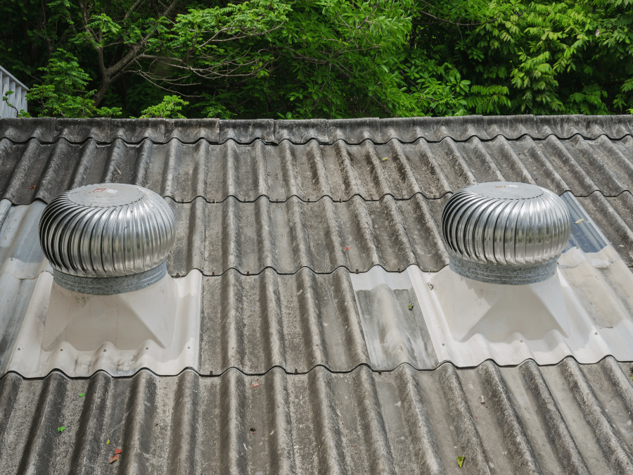 A roof with a vent on it and a building in the background.